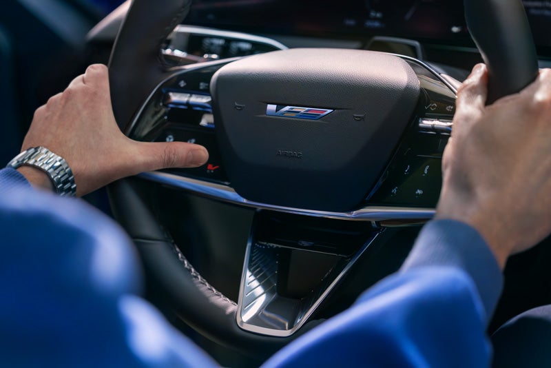 Close-up of a Man About to Press the V-Button on the 2026 OPTIQ-V Steering Wheel | Arnie Bauer Cadillac in Matteson IL